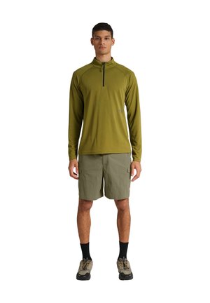 Mand står med front mod kamera iført olivengrøn langærmet trøje med lynlås, khaki cargoshorts, sorte sokker og vandresko på hvid baggrund.