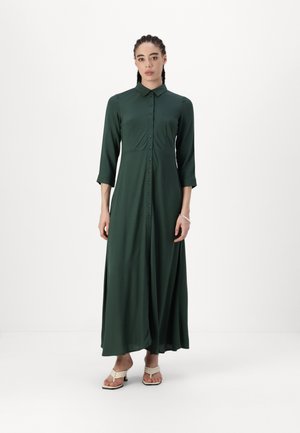 Robe longue verte fabriquée dans un tissu doux. Présente un devant à boutons, un col et des manches trois-quarts, avec une jupe fluide.