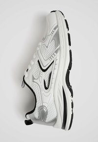 Baskets de sport blanches avec accents noirs et argentés, panneaux en mesh texturé, semelle épaisse et design à lacets vues de côté.