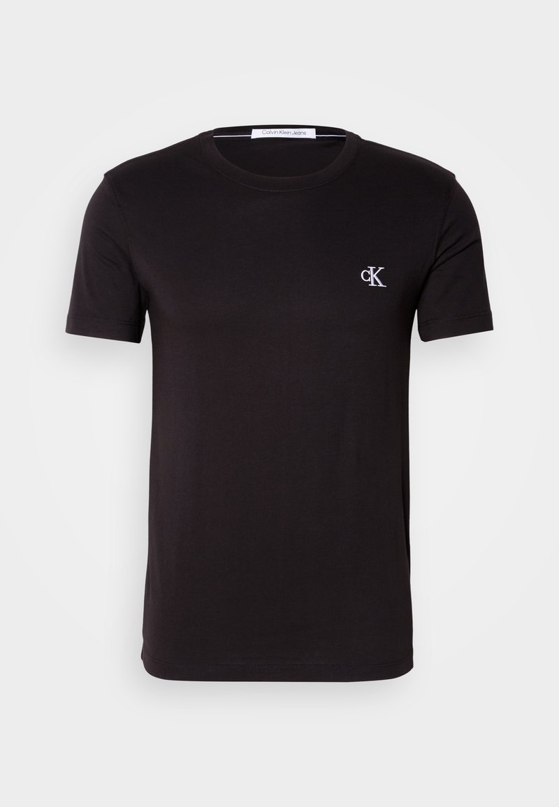 Camiseta negra de manga corta con cuello redondo, con pequeño logo blanco "cK" en el pecho izquierdo y etiqueta Calvin Klein Jeans en el interior del cuello.