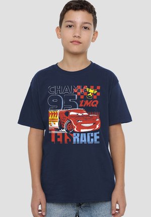 Boy wearing navy blue T-shirt with red race car and text "Champ 95 LMQ Let's Race" standing against plain background.