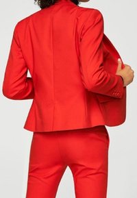 Červený oblek na míru se střiženým saka a kalhotami s rovnými nohavicemi. Hladká tkanina, strukturovaný design a knoflíkové detaily na saku.