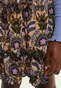 Blomsterprint nederdel i beige med bølget kant. Indeholder grønne, blå og pink mønstre; blødt stof; og et lagdelt design.