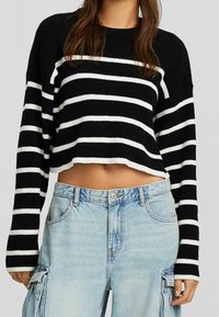Black and white striped cropped knit sweater with long sleeves, paired with light blue baggy jeans featuring side pockets.