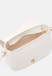 Bílá kožená crossbody kabelka s texturovaným povrchem, zlatým zipem a kulatým magnetickým zapínáním. Uvnitř se nachází kapsa na zip.