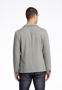 Grå ullblandning blazer med klassisk krage, två bakventiler och knapppartier på ärmarna, tillsammans med mörka denimjeans.