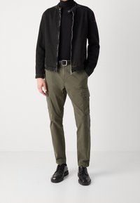 Černá denimová bunda se zipem vpředu, olivové cargo kalhoty s bočními kapsami a černé kožené boty, tvořící neformální outfit.