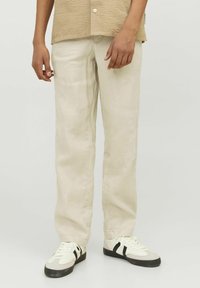 Crèmekleurige linnen broek met een rechte snit, met een gladde textuur. Gepaarde met witte sneakers met zwarte accenten. Casual outfit.