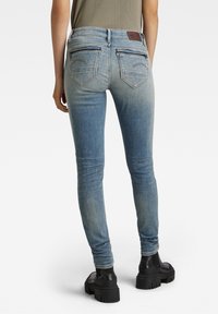 Jeans skinny in denim blu con aree scolorite, dettagli di cucitura sui taschini posteriori e una patch in pelle marrone in vita. Abbinati a stivali con tacco alto neri.