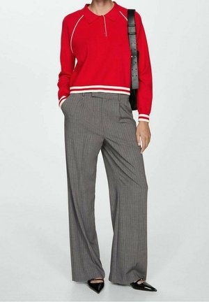 Personne portant un polo rouge à manches longues, un pantalon large à fines rayures grises, des chaussures pointues noires et un sac à bandoulière noir.
