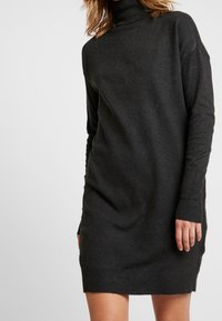 Tmavě šedé šaty s vysokým rolákem. Mají volný střih, dlouhé rukávy, žebrované manžety a lem, vyrobené z měkké pleteniny.