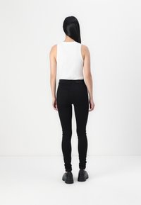 Jeans negros ajustados con una cintura alta, hechos de denim. Combinados con una camiseta sin mangas blanca ajustada y zapatos negros de suela gruesa.