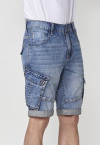 Lichtblauwe denim cargo shorts, voorzien van meerdere zakken, omgeslagen boorden en contrasterende stiksels. Gemaakt van stevige katoen.