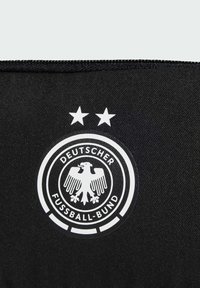 Black fabric with a smooth texture features a circular white logo. The logo has an eagle design, text, and two stars above it.