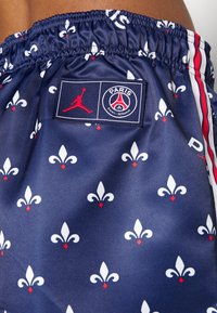 Pantaloni corti blu navy con motivo a fleurs-de-lis bianco e rosso, cintura elastica e patch con logo Jordan che presenta l'emblema del Paris Saint-Germain.