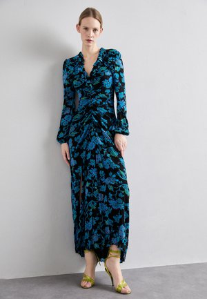 Rochie neagră cu motive florale albastre și verzi, mâneci lungi, cu un design pliat în față și fanta până la gleznă, asortată cu tocuri verzi cu curele.