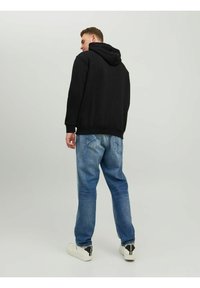 Zwarte hoodie gecombineerd met lichtblauwe denim jeans. De hoodie heeft een comfortabele pasvorm; de jeans hebben achterzakken en een vervaagd uiterlijk.
