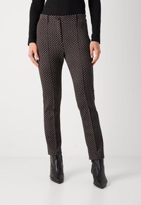 Pantalons noirs à motif avec un design texturé et une impression discrète, associés à des bottes à talon pointues noires.