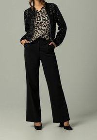 Zwarte sequined bomberjack, blouse met luipaardprint en zwarte broek met brede pijpen en zakken. Zwarte hakken maken de outfit compleet.