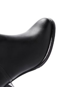 Bottine noire avec une finition en cuir lisse, bout arrondi et talon bas texturé. Présente des lignes épurées et un design minimaliste.