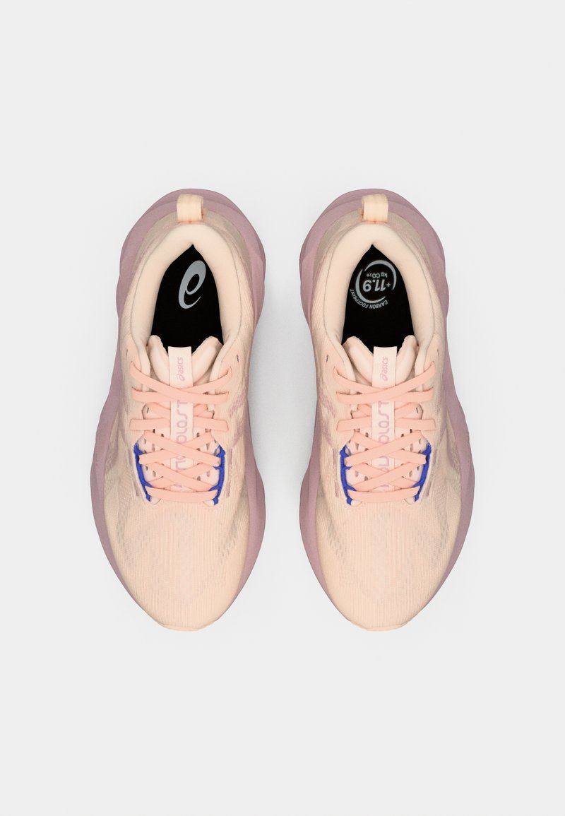 Baskets de sport roses clairs avec une tige texturée, des lacets violets contrastants et une languette rembourrée. Comprend une semelle intérieure noire avec un logo.