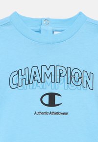 Φωτεινό γαλάζιο μπλουζάκι με στρογγυλή λαιμόκοψη, με έντονο μαύρο κείμενο και λογότυπο "CHAMPION". Μαλακό βαμβακερό υλικό, απλός σχεδιασμός, χωρίς σχέδια ή διακοσμητικά στοιχεία.