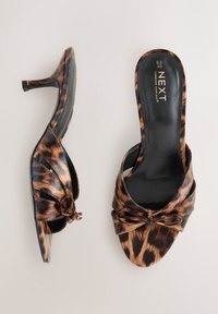 Sandales à talons imprimé léopard avec un détail noué à l'avant, bout ouvert et talon fin. Fabriquées en matériau brillant avec une texture lisse.