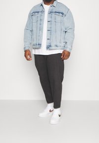 Vaaleansininen farkkutakki, jossa on kaksi rintataskua ja näkyvät saumat, päällä valkoinen T-paita ja tummat housut, yhdistettyinä valkoisiin lenkkareihin.