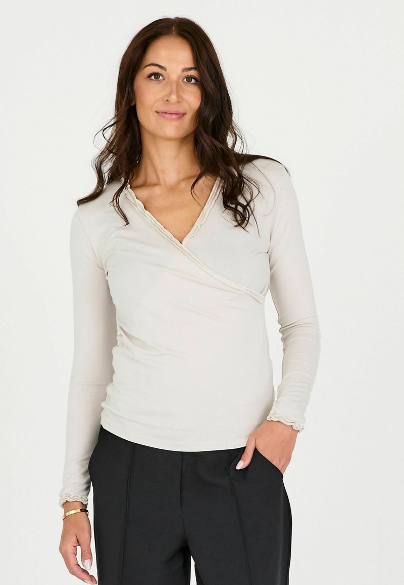 Top avvolgente beige chiaro con maniche lunghe, presenta uno scollo e polsini a onde. Realizzato in tessuto morbido, è caratterizzato da una silhouette aderente.