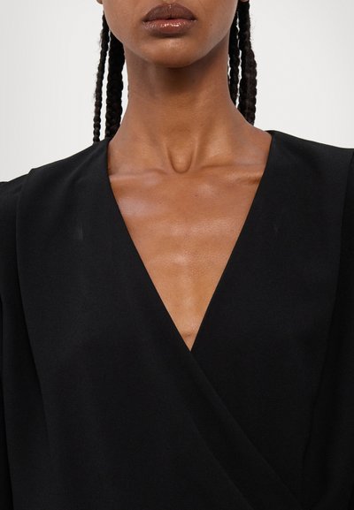 Black wrap blouse featuring a deep V-neckline with smooth fabric, structured shoulders, and subtle sheen, highlighting a minimalist design.