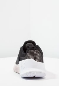 Sneaker atletica in bianco e nero con upper in rete e suola testurizzata, mostrata da dietro su una superficie bianca contro uno sfondo bianco angolare.
