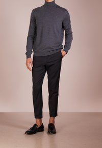 Grå polotröja i mjukt stickat material, kombinerad med svarta skräddarsydda byxor och blanka svarta loafers, visad mot en ljus bakgrund.