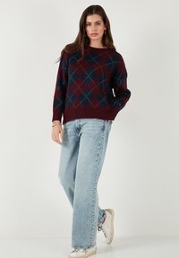 Pull en tricot argyle bourgogne et bleu marine avec un col rond et une coupe décontractée, associé à un jean large bleu clair et des baskets blanches.