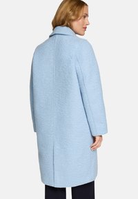 Manteau texturé bleu clair avec col, coupe droite, manches longues et détails de couture au dos. Apparence de tissu lisse.