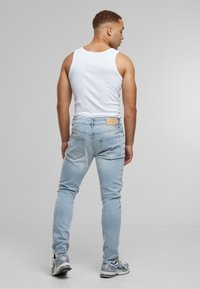 Light blue skinny jeans with a faded finish and two back pockets, paired with a white tank top and gray athletic shoes.
