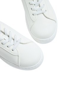 Sneakers bianchi in pelle con punte rotonde, lacci bianchi piatti e dettagli cuciti lungo la suola. Texture liscia e design minimale.