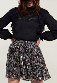Schwarze Bluse mit Spitzenakzenten und Rüschensäumen, kombiniert mit einem gemusterten Rock, der bunte Blumenmuster auf dunklem Hintergrund zeigt.