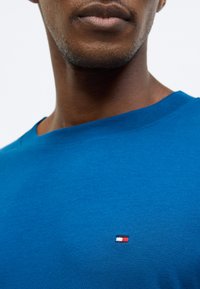 Μπλε βαμβακερό μπλουζάκι με στρογγυλή λαιμόκοψη και μικρό κεντητό λογότυπο σε κόκκινο, λευκό και μπλε στην αριστερή πλευρά του στήθους. Λεία υφή.