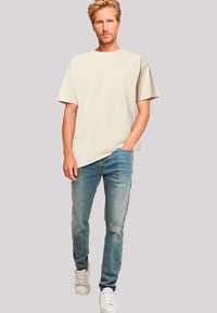 Beige short-sleeve t-shirt paired with light blue distressed jeans. Shoes are white sneakers. Simple, casual design with a relaxed fit.