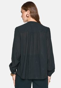 Blusa nera leggera con maniche lunghe a sbuffo, motivo floreale ricamato e cucitura posteriore arricciata, con polsini abbottonati.