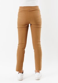 Pantaloni marroni slim fit con una texture liscia e una vita media, caratterizzati da una silhouette aderente e spacchi laterali all'orlo. Indossati con sneakers bianche.