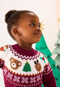 Pull en tricot avec un empiècement bordeaux orné de motifs festifs multicolores comme un ours, un renne, un sapin de Noël et des flocons de neige sur une base blanche.