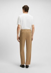 Beige byxor med rak ben, tillverkade av ett slätt tyg. Har två bakfickor och en subtil midjeband, kombineras med en vit skjorta.