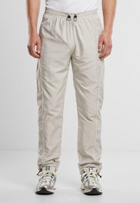Lichtbeige joggingsbroek met een elastische tailleband, koord, zijzakken en witte piping langs de naden, gemaakt van gladde, lichte stof.