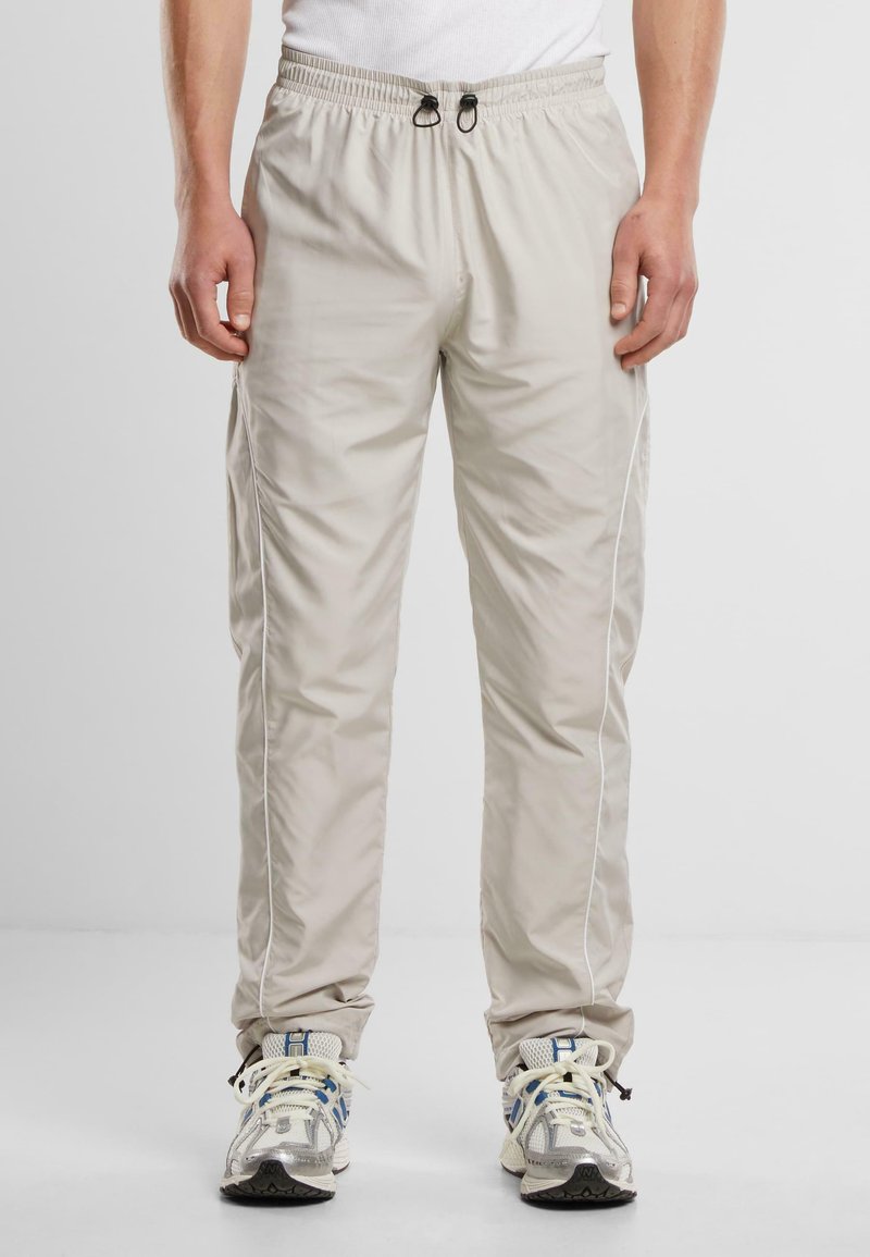 Lichtbeige joggingsbroek met een elastische tailleband, koord, zijzakken en witte piping langs de naden, gemaakt van gladde, lichte stof.