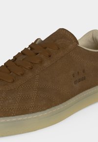 Baskets en daim marron avec une semelle beige épaisse, des lacets marron assortis et des détails cousus subtils sur le côté.