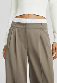 Pantalones plisados de color gris claro con una cinturilla elástica blanca, que presentan una textura suave y un detalle de bolsillo en la parte frontal.