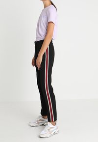 Svarta byxor med röda och vita sidopaneler, kombinerat med en lavendelfärgad t-shirt. Bärs med mångfärgade sneakers för att skapa en avslappnad look.