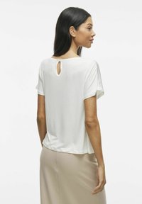 Hvit kortermet topp med rund hals og nøkkelhull i ryggen. Laget av mykt stoff, med et avslappet snitt og jevn tekstur.