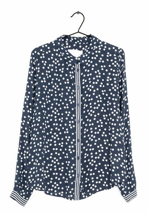 Laivastonsininen, pitkähihainen napitettava paita valkoisilla pilkuilla, raidallinen napituslista ja raidalliset kalvosimet, ripustettuna mustalle henkari.